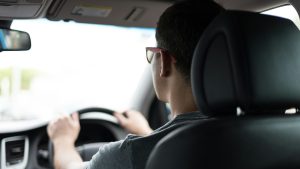 Man met zonnebril rijdt auto en kijkt gefocust vooruit tijdens het rijden