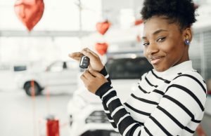 Vrouw glimlacht terwijl ze autosleutels toont bij een nieuwe auto, symbool voor behalen van rijbewijs of aankoop.