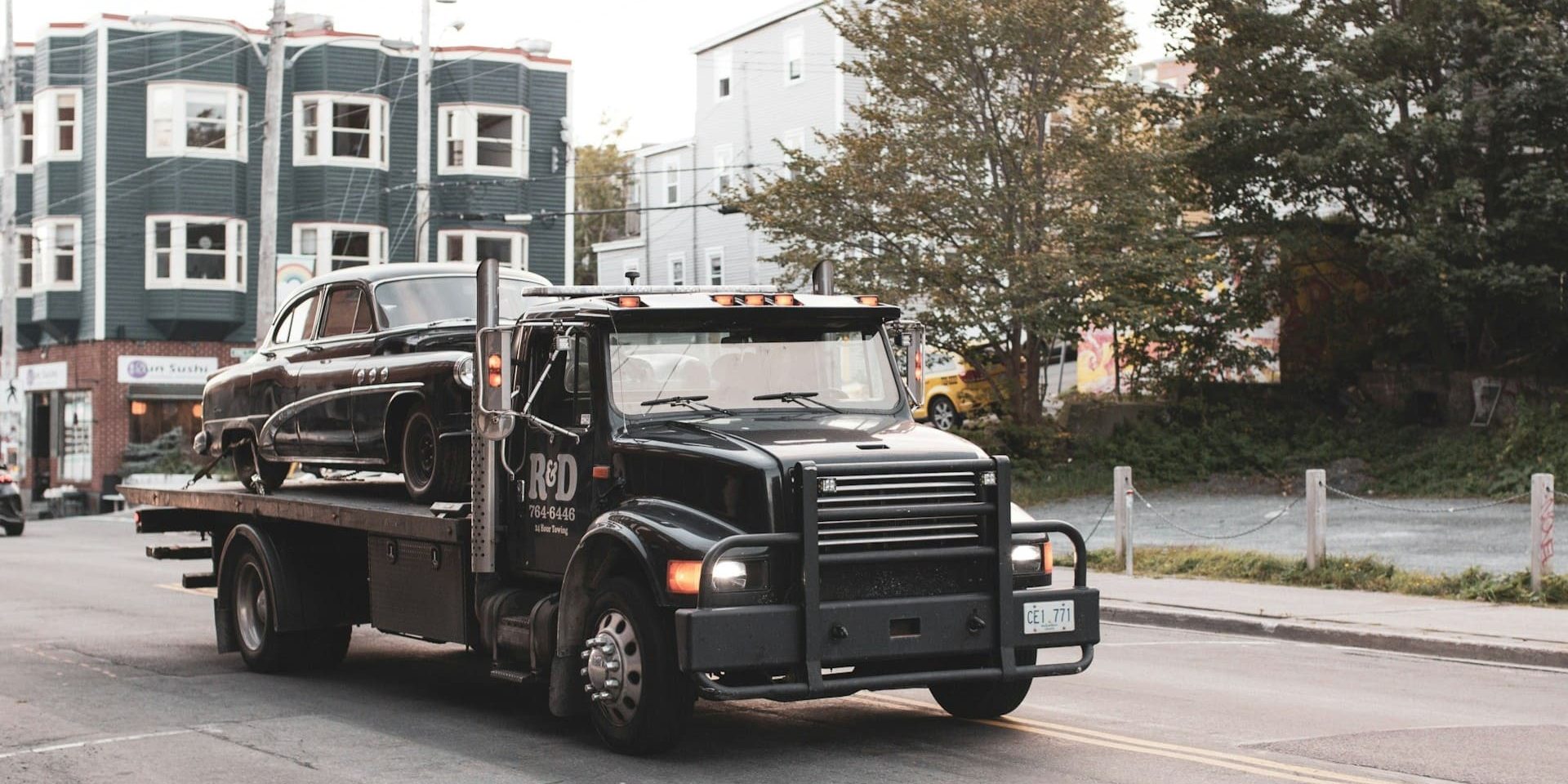 takelbedrijf Een zwarte takelwagen vervoert een klassieke zwarte auto door een stadsstraat.