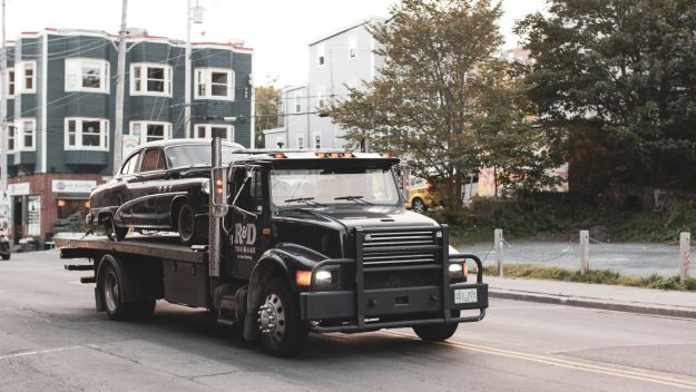 takelbedrijf Een zwarte takelwagen vervoert een klassieke zwarte auto door een stadsstraat.