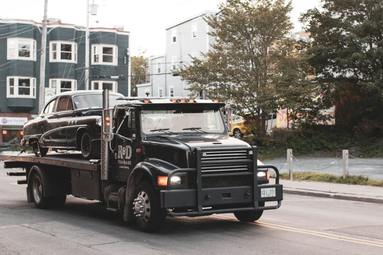 takelbedrijf Een zwarte takelwagen vervoert een klassieke zwarte auto door een stadsstraat.