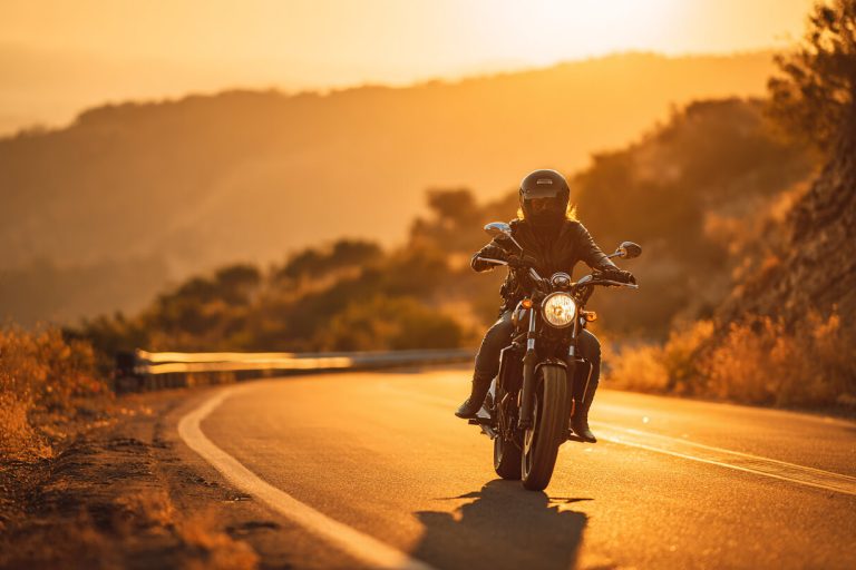 Motorrijder rijdt bij zonsondergang over een bochtige weg met aandacht voor nek en onderrug.